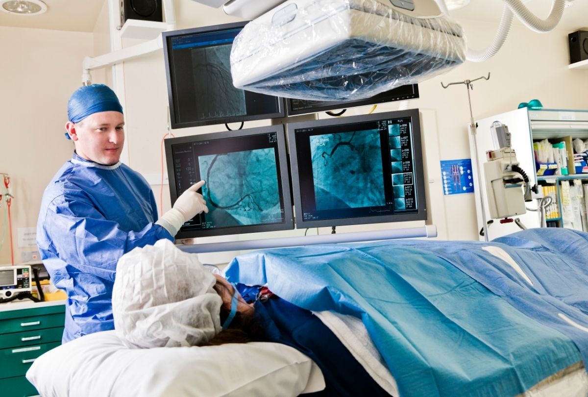cath lab landing page Cardiologist talking with patient and pointing to heart images, while patient lays on guerney